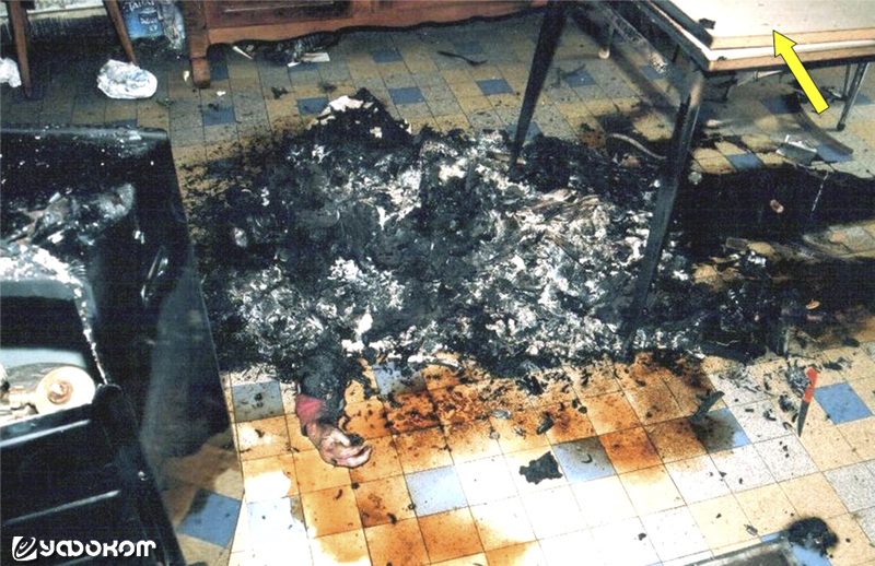 Рисунок 1. Жертва 1: тело, превратившееся в фрагменты и пепел, обнаружили на полу кухни, частично под столом, в положении лежа на спине. Стрелка показывает на хорошо сохранившийся кухонный стол.