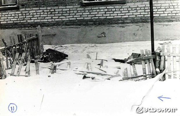 Фото 11. Разрушенный штакетник крупным планом. Под снегом виднеется крышка люка. Слева короткий отрезок забора, примыкающий к дому, тоже несёт следы разрушения. Стрелка – кусок шифера в снегу. (Фото Макарова В.Н.).